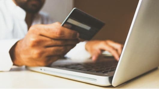 A man behind a laptop is holding a credit card.