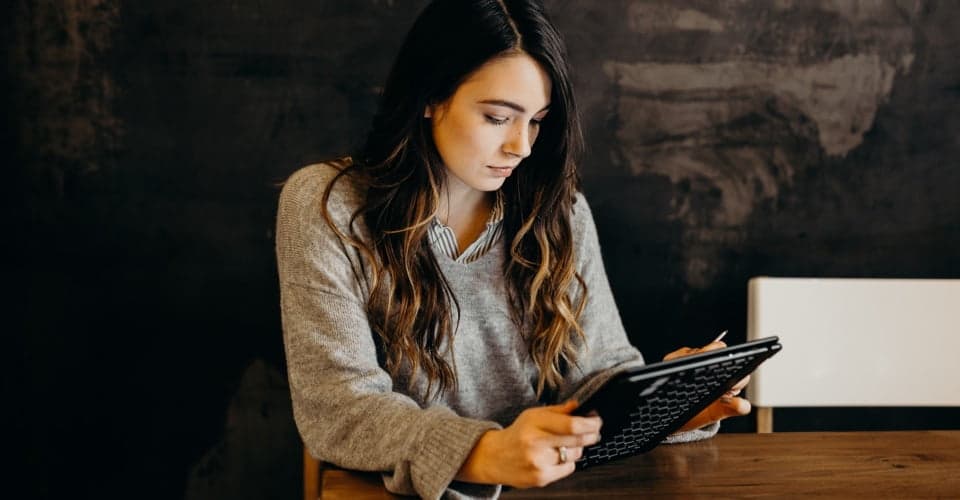 Young lady sitting at the table looking at a tablet screen.